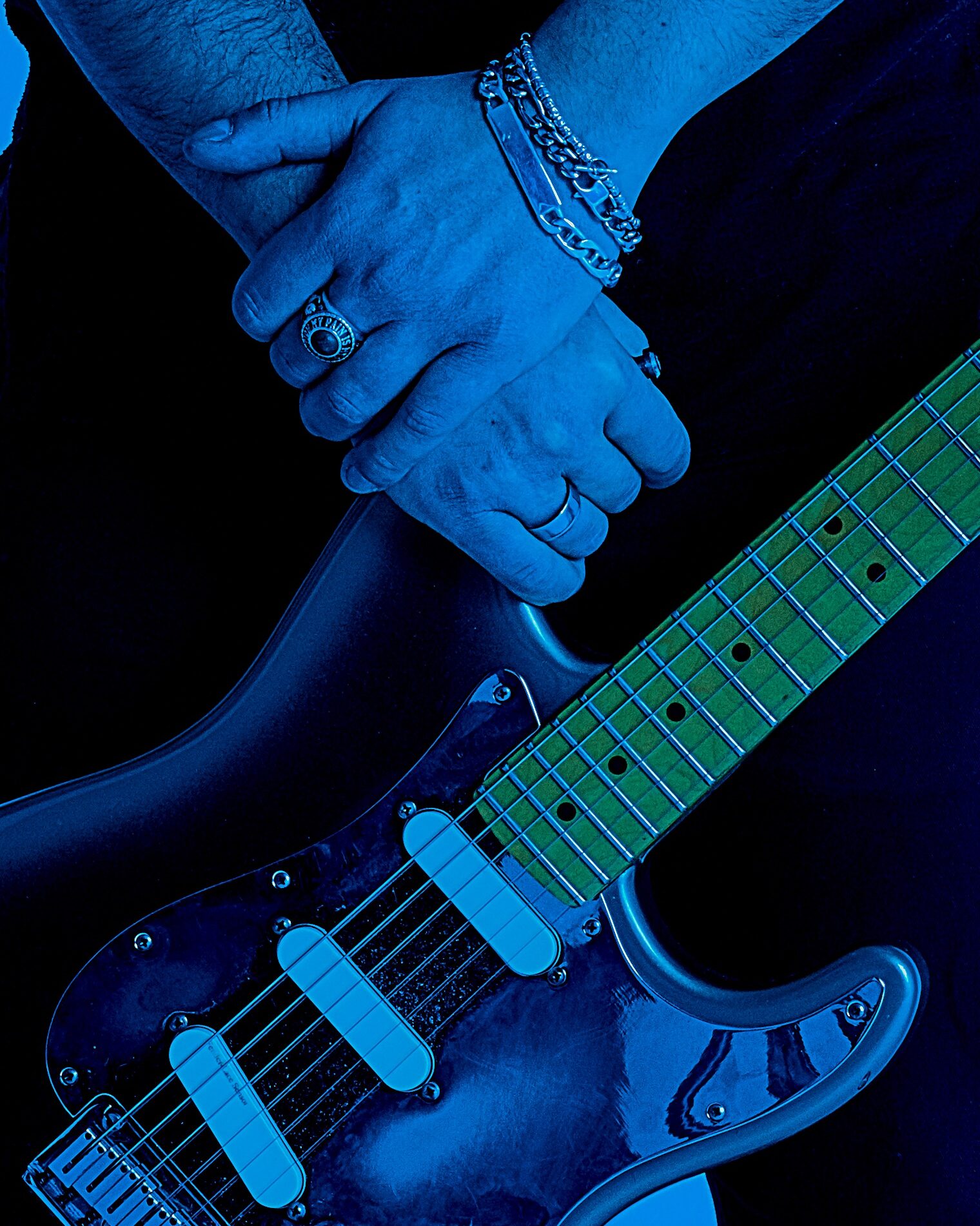 mani congiunte che tengono una chitarra elettrica la luce è blu spiccano i dettagli metallizzati dei gioielli e della chitarra