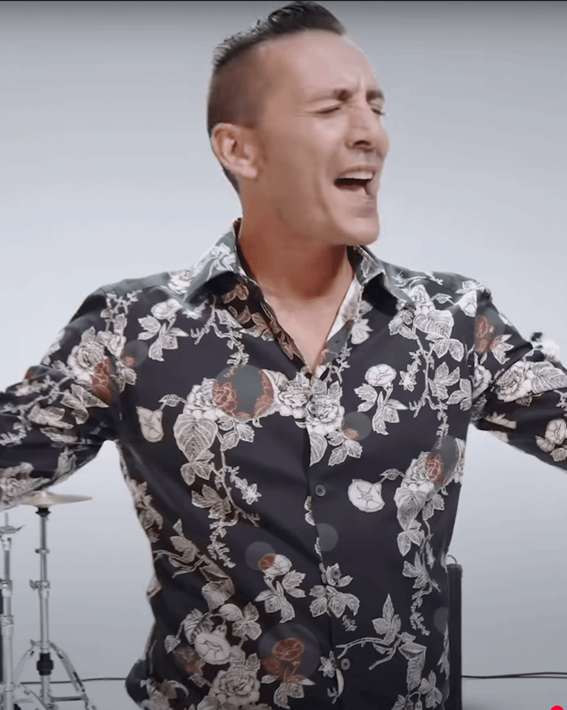 kekko dei modà che canta a braccia aperte indossa una camicia a fiori di scena immagine presa dal videoclip testa o croce
