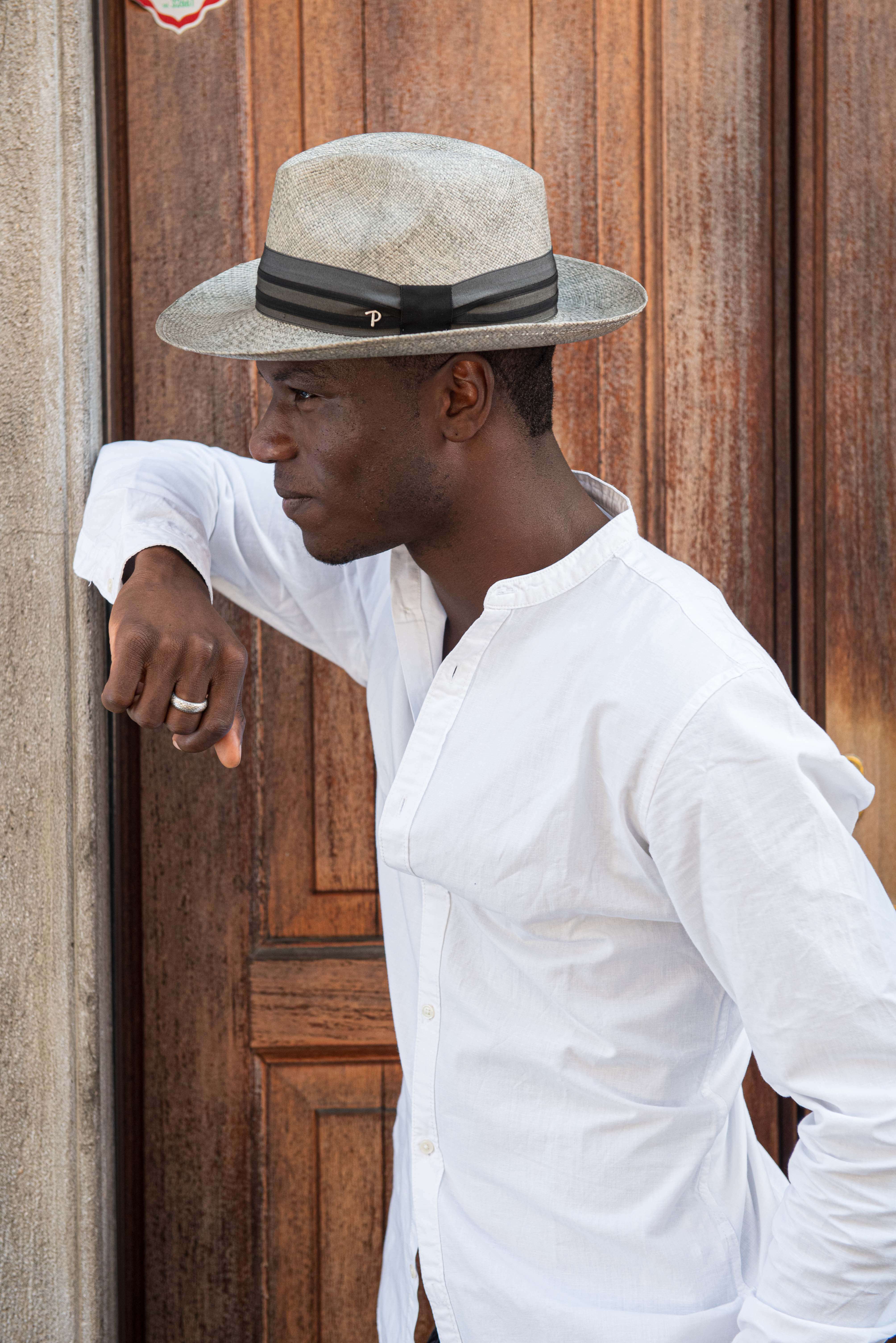 modello indossa cappello panizza color tortora mentre è appoggiato allo stipite di pietra di un portone