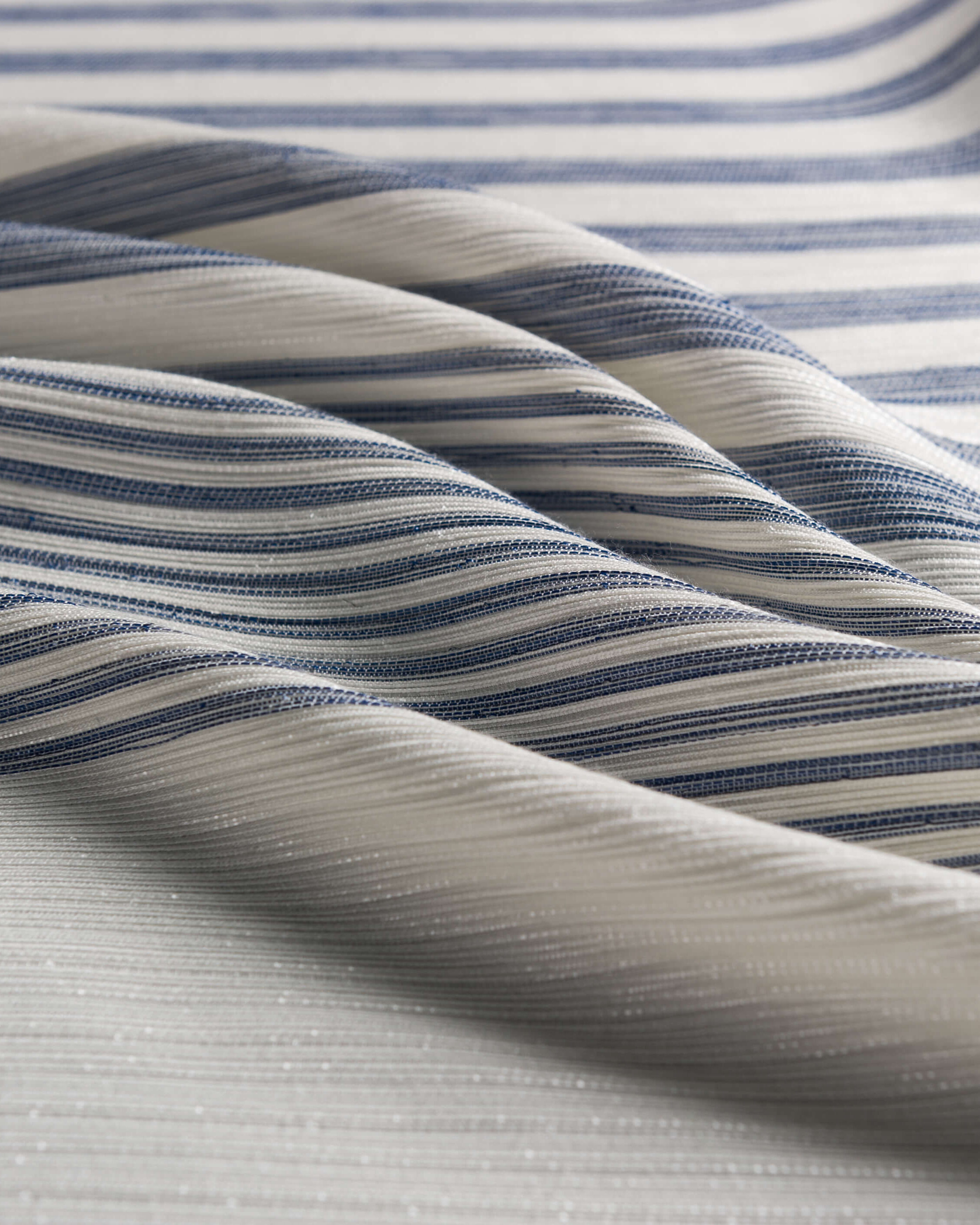 Tessuto con intrecciatura lineare bianco a righe irregolari blu appoggiato con pance morbide e parallele