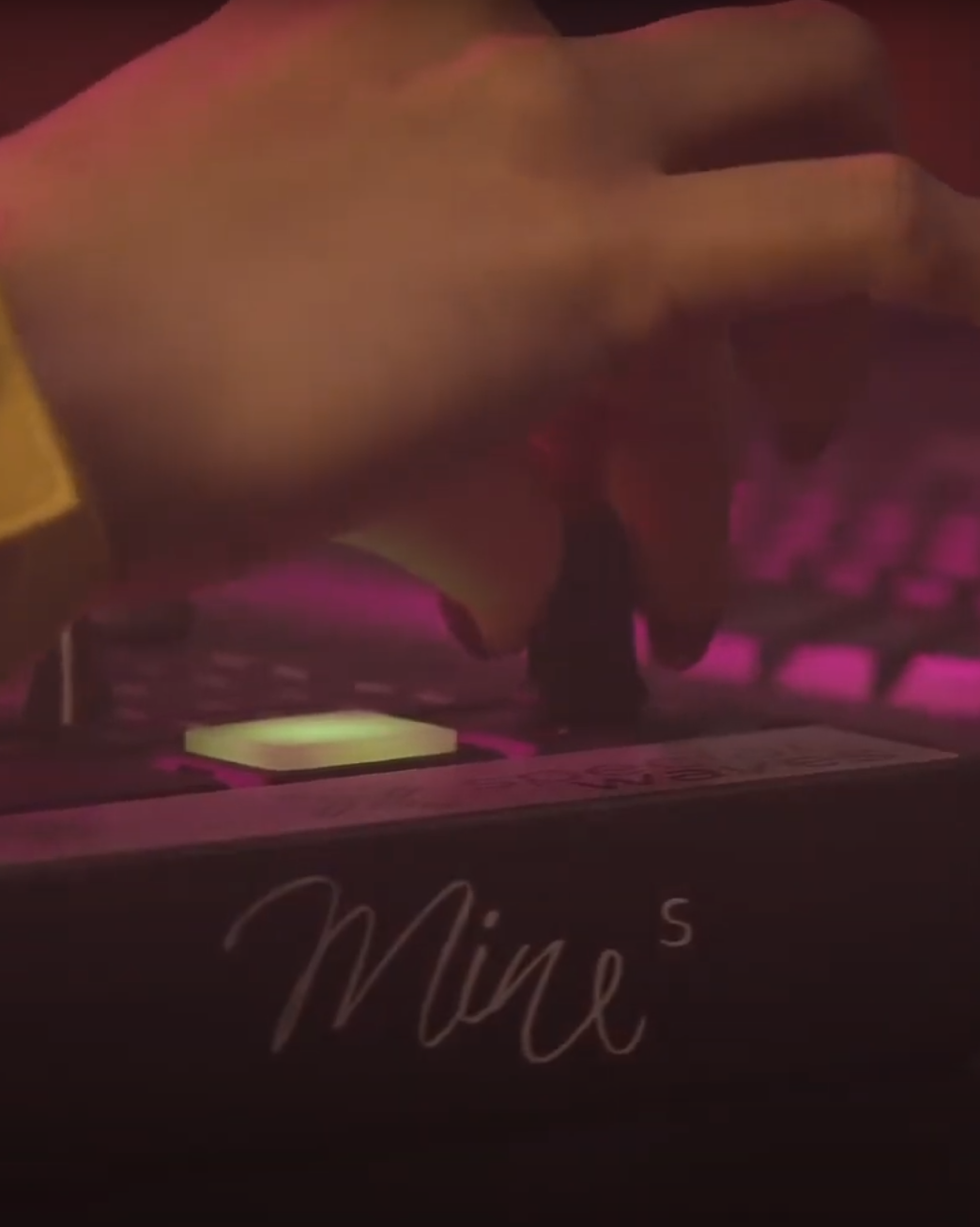 una mano che muove un regolatore di volume di un mixer durante un Live con luci colorate