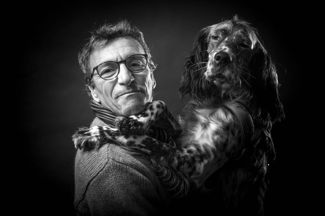 un uomo con occhiali e sciarpa tiene in braccio il suo cane in una posa elegante