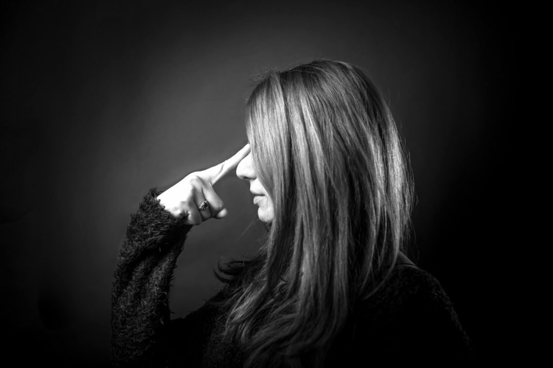 ragazza fotografata di profilo i capelli svelano solo naso bocca e mento con l'indice della mano destra sembra voler nascondere la linea creata dal naso